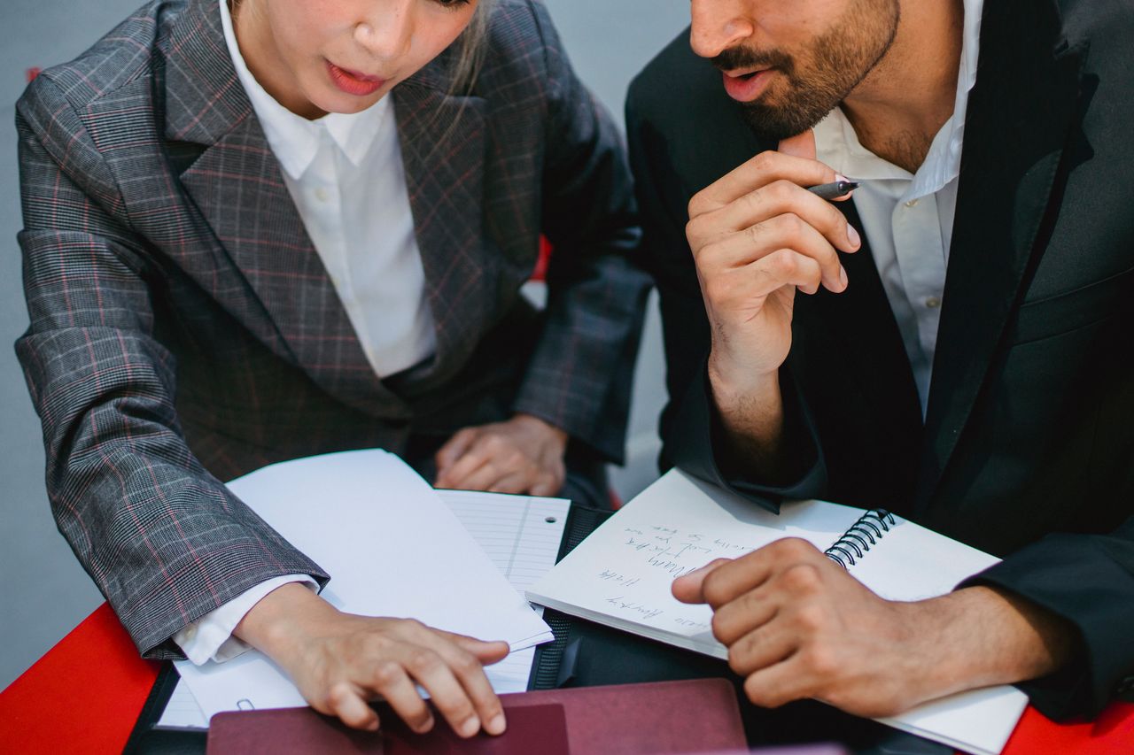 Two business professionals discussing plans with notebooks and papers at a meeting.